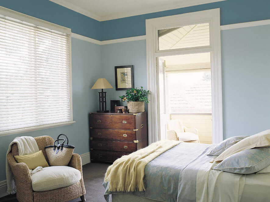 Blue Bedroom with dark wooden drawers and chair with blue bedding and pillows
